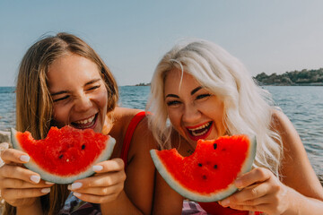 Watermelon Beach Summer: Two women joyfully eating watermelon slices on sunny beach.