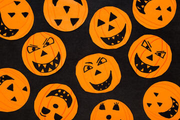 Orange scary smiling pumpkin faces on dark black table background. Closeup. Creating Halloween decoration. Little child handcraft. Top down view.