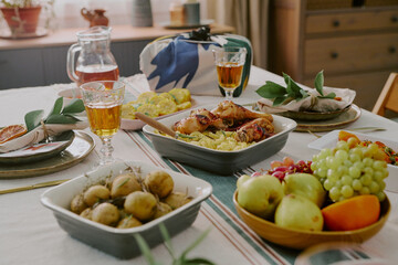 Closeup showing festive table set for Kwanzaa celebration with traditional dishes including roasted chicken, potatoes, fresh fruit, napkins folded with green leaves, glasses of juice