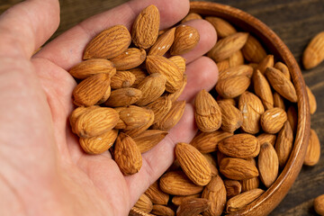 whole and unroasted almonds in a person's hand, a large amount of hard raw almonds is held in the hand against the background of other nuts