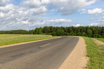 a narrow paved road in rural areas in the summer with cloudy weather and a sky with lots of clouds, a country road covered with asphalt