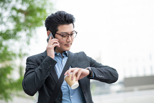 Businessman on phone checking time on watch outdoors