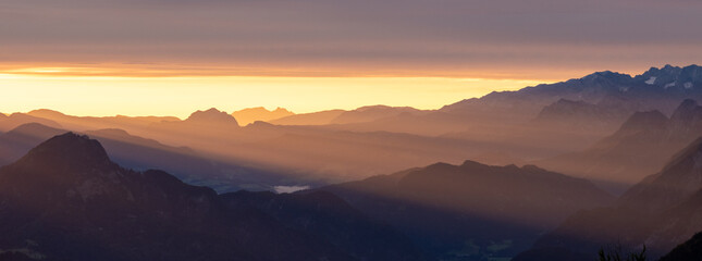 Panoramic alpine sunset with layered mountain silhouettes and glowing horizon