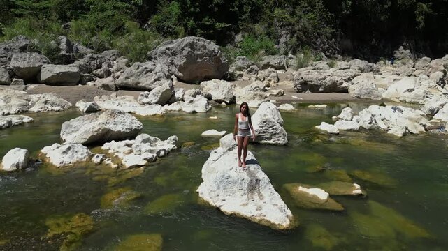 A woman balances on a rock at Tinipak River, striking a graceful pose before blowing a flying kiss as the drone pulls away&mdash;capturing both elegance and raw natural beauty.
