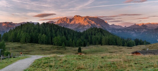 Panoramic alpine meadow at sunset in the Berchtesgadener Alps with wooden hut and glowing mountain peaks