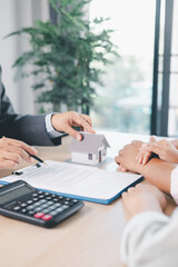 Close up of real estate agent showing small house model to client with calculator, contract paperwork on desk, concept of mortgage loan, home ownership, property investment agreement. mortgage loan