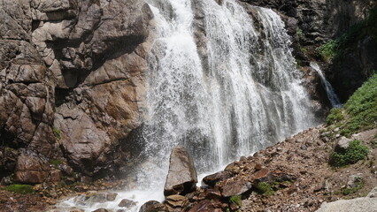 Cascading pure white water rushes down rugged granite cliffs, surrounded by dense vegetation that emphasizes nature's raw beauty and power