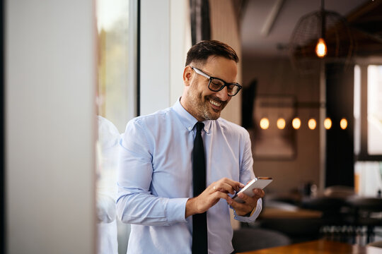Happy businessman texting on cell phone in cafe. - Powered by Adobe