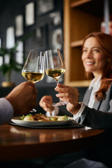 Close up of coworkers toasting with wine during business lunch in restaurant.