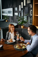 Happy businesswoman and her coworker toasting with wine during meal in restaurant.