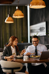 Happy entrepreneurs using computer while having business lunch in restaurant.