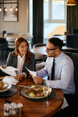 Happy entrepreneur and her coworker analyzing business reports during lunch in restaurant.
