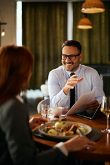Happy businessman communicating with female colleague during lunch in restaurant.