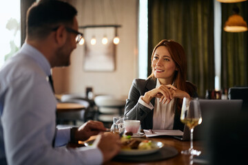 Happy entrepreneur talking to coworker while having business lunch in restaurant.