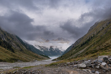 Moody alpine valley trail in the Zillertal Alps, dramatic clouds rolling through green mountain slopes, remote hiking landscape with changing weather in the Austrian Alps
