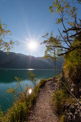 Scenic lakeside hiking trail along Lake Achensee with turquoise water, sunlit path and alpine landscape, peaceful outdoor adventure in the Austrian Alps