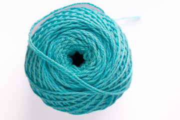 Turquoise knitting yarn for hand knitting, wound on a spool with diagonal threads on a white background