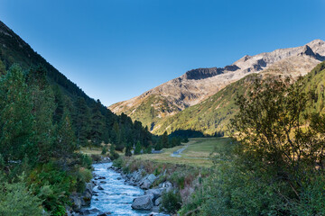 Zamser Bach mountain stream flowing through green alpine valley, clear water and rugged peaks under blue sky, peaceful high mountain landscape in Tyrol, Austria