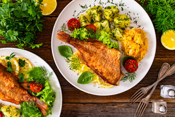 Fried atlantic redfish with boiled potatoes and sauerkraut on wooden table. Top view