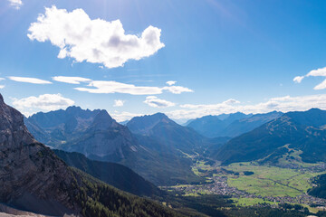 Naklejka premium Wide alpine mountain view from the Gamskar overlooking the valley of Ehrwald, rugged rocky slopes, green forests and distant peaks under clear blue sky