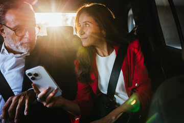 Two business professionals discussing over a smartphone inside a vehicle
