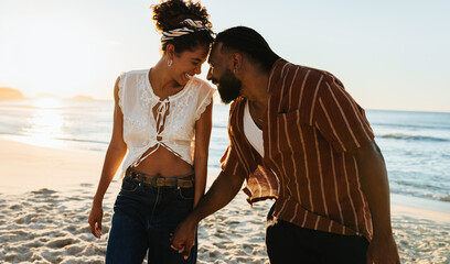 Cute couple laughing and holding hands on a sunny beach stroll