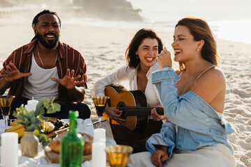 Friends singing together at a beach picnic during sunset