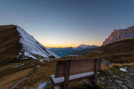 Wooden bench overlooking the R&auml;tikon at sunset, quiet alpine pass with rolling hills, distant peaks and soft evening light creating a peaceful mountain mood