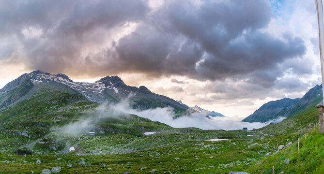 Dramatic alpine landscape in the Zillertal with lush green meadows, low drifting clouds and heavy storm sky, remote high mountain scenery with changing weather