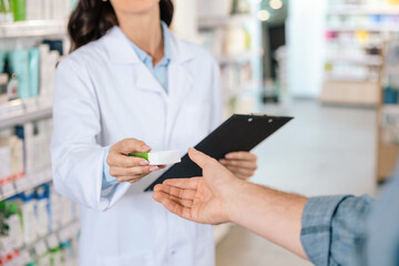 Unrecognizable woman pharmacist giving medicine to male client