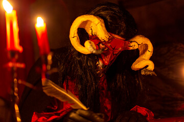 A scary person in a devil or demon costume with large horns, lit by candlelight. A terrifying and atmospheric image perfect for Halloween, horror, and fantasy themes.