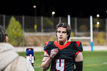 American football player in jersey standing on a sports field under stadium lights, giving an...
