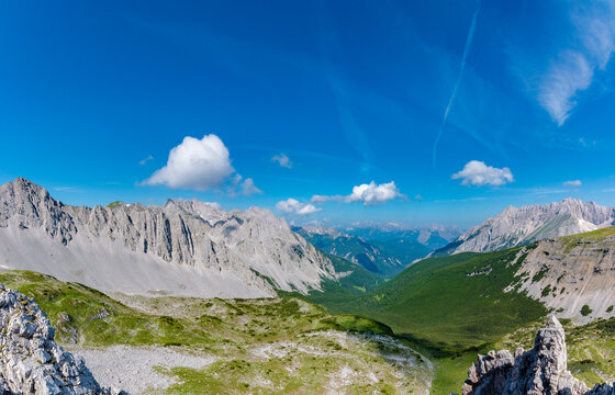 Panoramic view from the Goetheweg into the Karwendel Mountains with wide alpine valley, rugged limestone peaks and deep blue summer sky