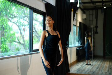 Graceful ballerina standing near window with eyes closed in elegant ballet pose