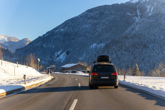 Scenic back view family van car roof box rack luggage drive alpine countryside road cold winter day Europe mountain resort. Automobile vehicle holidays trip journey. Vacation transport seasonal scene