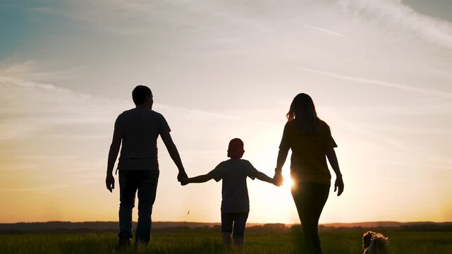 Walking family holding hands toward sunset silhouette of parent and child in open field sun low on horizon long shadow casual clothing walking together holding hand calm connection nature glow orange