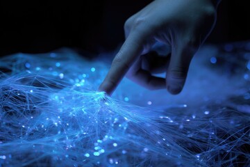 Close-up of a hand touching glowing, web-like fibers in blue tones, dark background