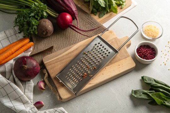 Fresh vegetables and herbs arranged around a stainless steel grater on a wooden cutting board