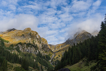 mountain landscape with two big main peaks in front an vertical forest and rainy clouds on blue sky