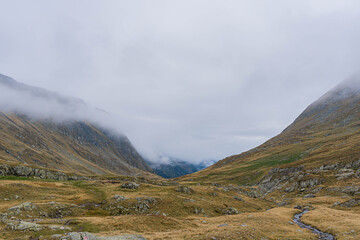 lunar scottish look autumn colored landscape in carpathian valley with low big white clouds ahead
