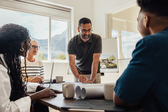 Architectural team meeting discussing design plans with diverse members at an office table