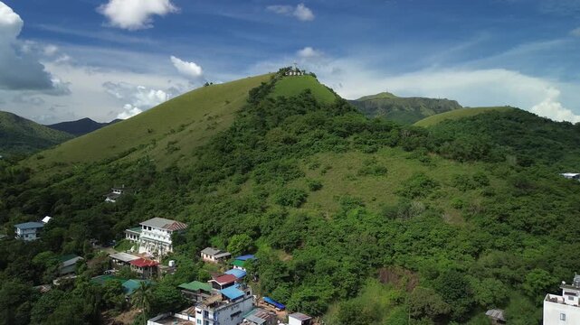 Wide aerial view of green slopes below Mount Tapyas in Coron with hillside buildings forested ridges summit structures and dramatic daylight clouds over Palawan