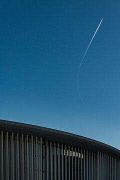 View of a modern philharmony, curved building facade of grey vertical panels against a stark blue sky with a jet stream cutting diagonally across, Luxembourg city, Luxembourg.