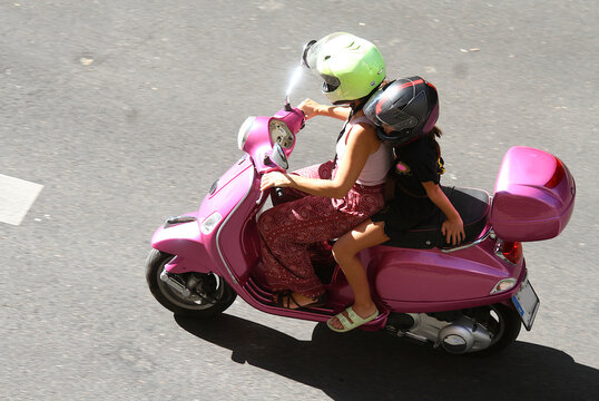 Moto rosa con ba&uacute;l top case con madre e hija de conductora y acompa&ntilde;ante paquete con casco por la carretera de las calles de Madrid