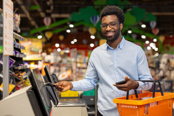 Young african man smiling as he completes a contactless credit card payment with his smartphone at...