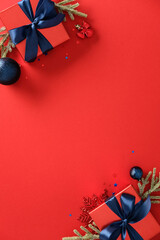 Christmas vertical banner, poster design. Top view red gift boxes with blue ribbons, baubles, fir branches on red background