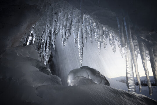 View of glistening icicles hang like frozen daggers, framing the rush of water as it cascades over icy formations, creating a surreal and ethereal landscape, Iceland.