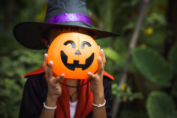 Two young children in Halloween costumes stand outdoors, holding pumpkin buckets with...