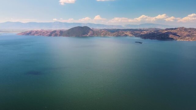 aerial perspective of Bafa Lake in Turkey, showcasing its tranquil blue waters, surrounding mountains, and the unique landscape shaped by both nature and ancient history. This footage captures the ser