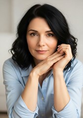 Fototapeta premium Portrait of a beautiful middleaged woman with dark hair and brown eyes, looking directly at the camera with a gentle smile and hands clasped in front of her face